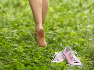 woman walking barefoot in grass with pink shoes laying behind her